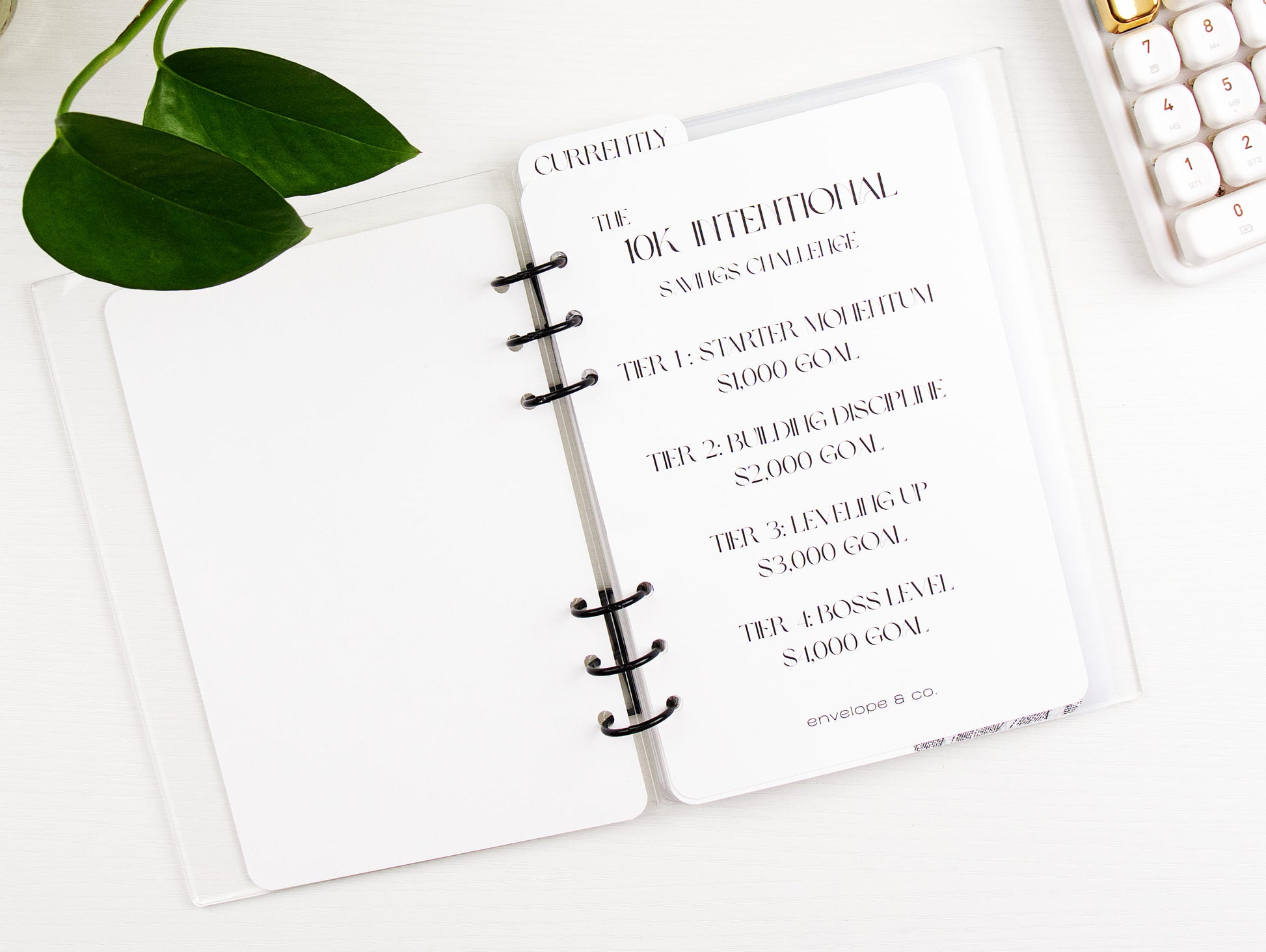 Binder with a goal-setting list on a white surface with a keyboard and plant.
