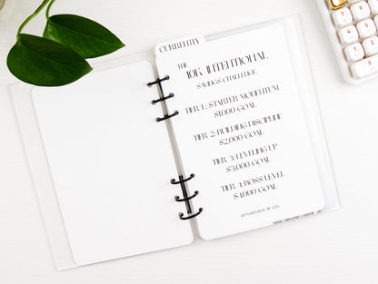 Binder with a goal-setting list on a white surface with a keyboard and plant.