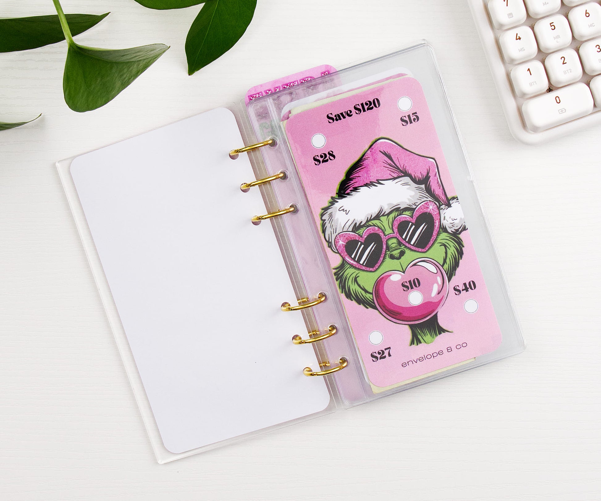 Binder with a pink-themed savings challenge on a white surface with a calculator and plant.