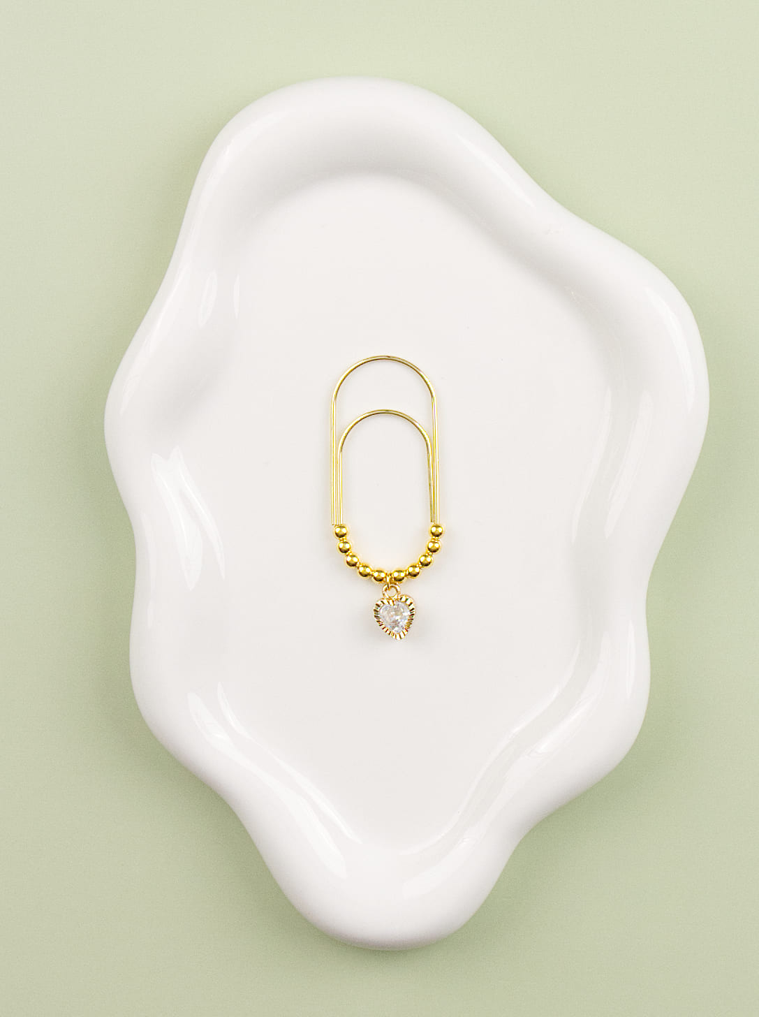 Gold charm with a small crystal heart on a white dish against a light green background