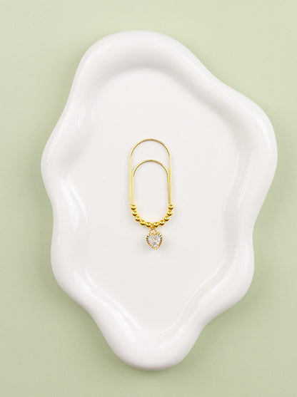 Gold charm with a small crystal heart on a white dish against a light green background