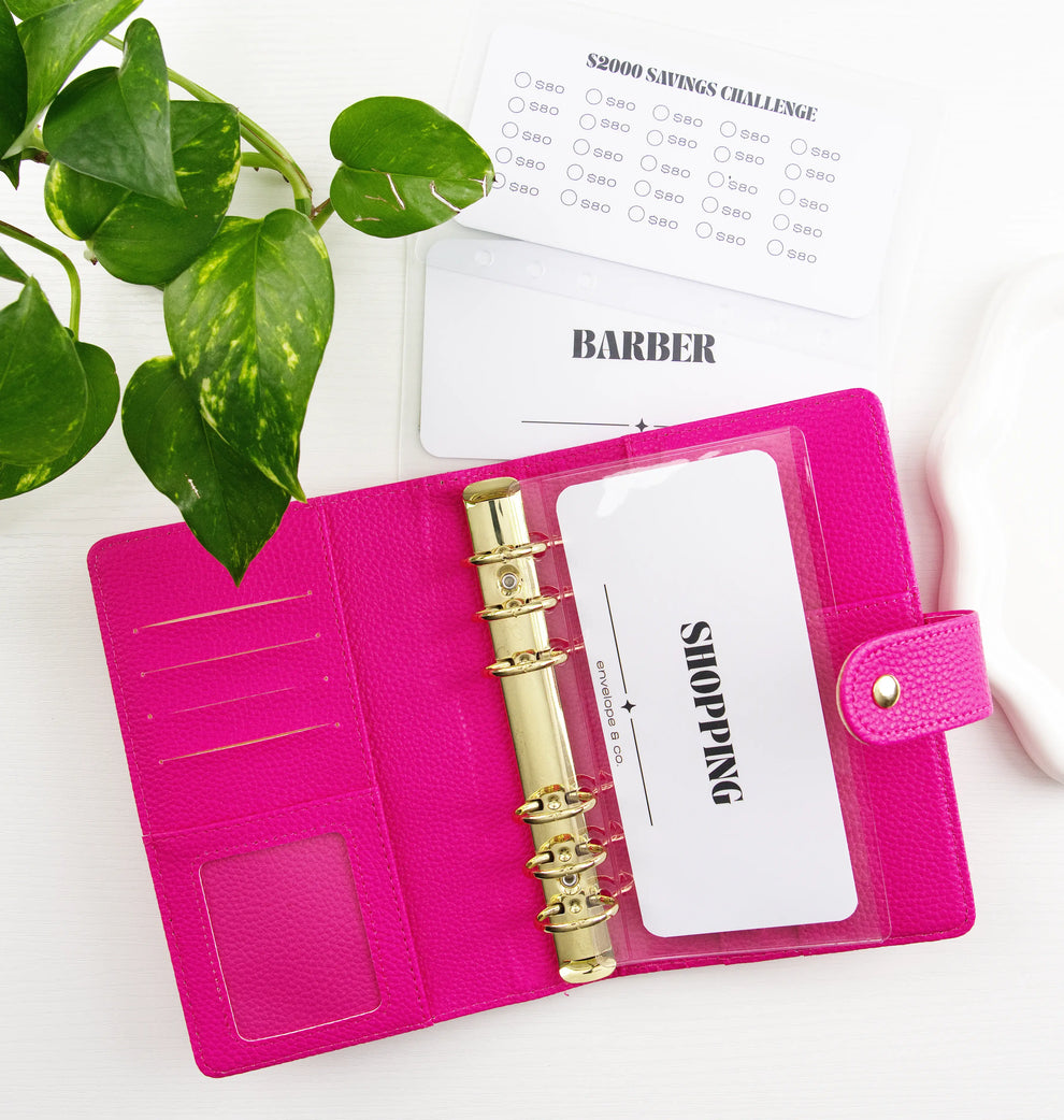 Pink binder with gold hardware and white inserts on a white surface with a plant.
