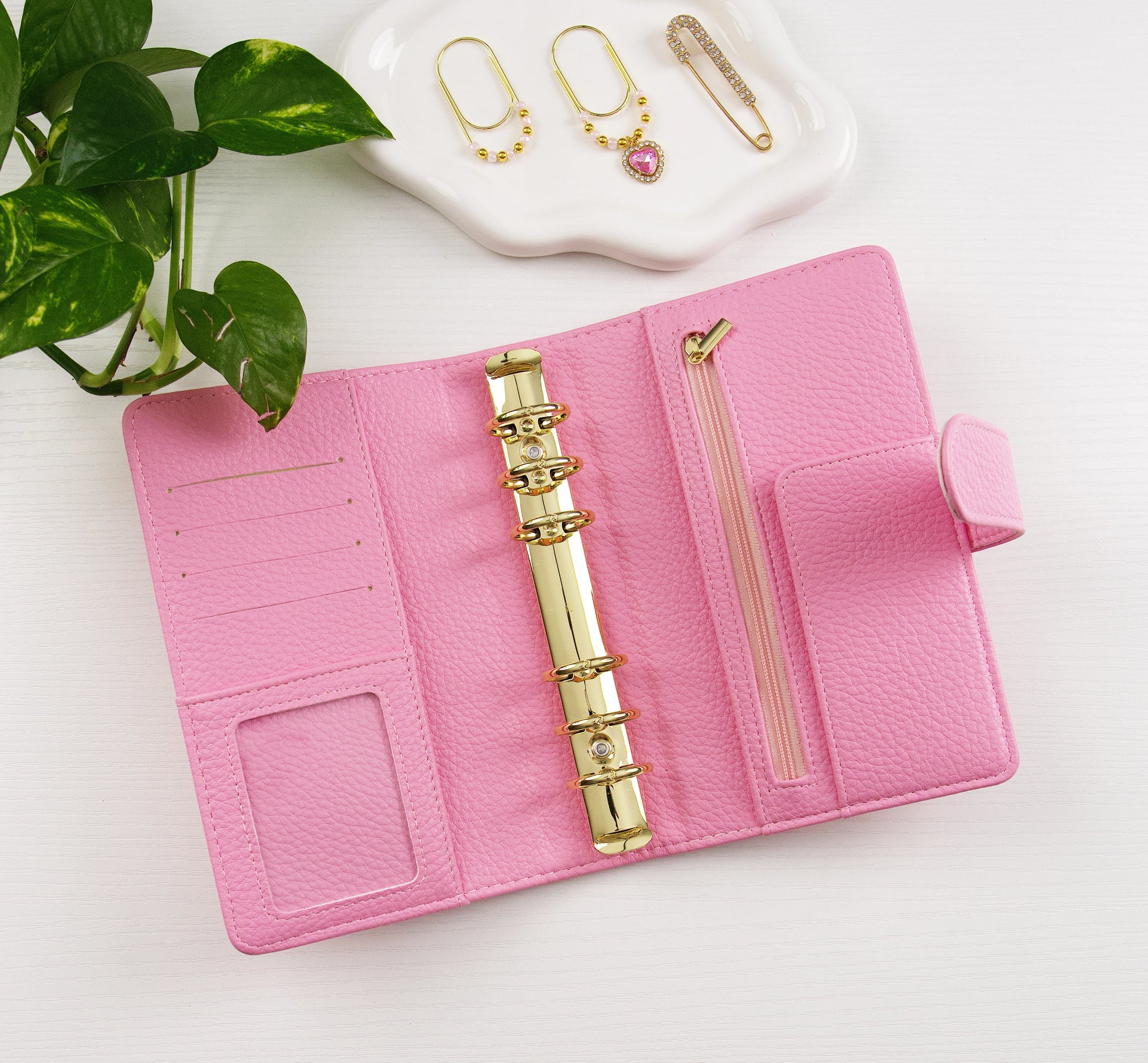 Pink binder with gold accents on a white surface, with earrings in the background.