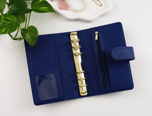 Navy blue binder with gold binding on a white surface with a plant in the corner