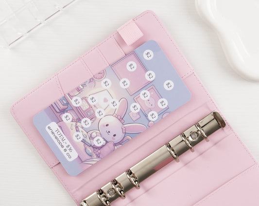 Kawaii bunny savings tracker with $2 increments totaling $36 in pink vegan leather binder with silver rings on white background