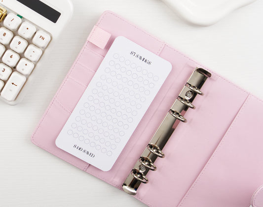52-week savings challenge tracker with minimalist circle design in pink leather binder with silver hardware and decorative safety pin
