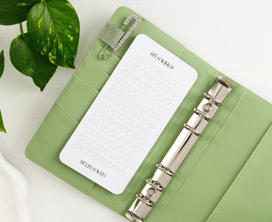 $15 Savings tracker with minimalist circle grid in sage green binder with silver rings and decorative safety pin showing $220 savings goal