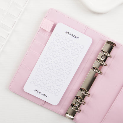 Minimalist $15 Savings tracker with circle grid design in pink leather binder with silver rings showing $1320 savings goal