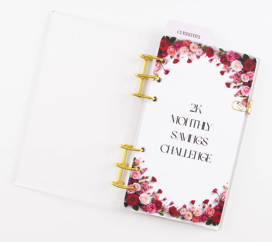 Clear acrylic A6 binder with gold 6-ring hardware featuring floral design and 2K Monthly Savings Challenge text on white background