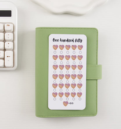 One Hundred Fifty dollar savings tracker with 30 ice cream waffle cone hearts at $5 each displayed on top of a sage green binder on white background